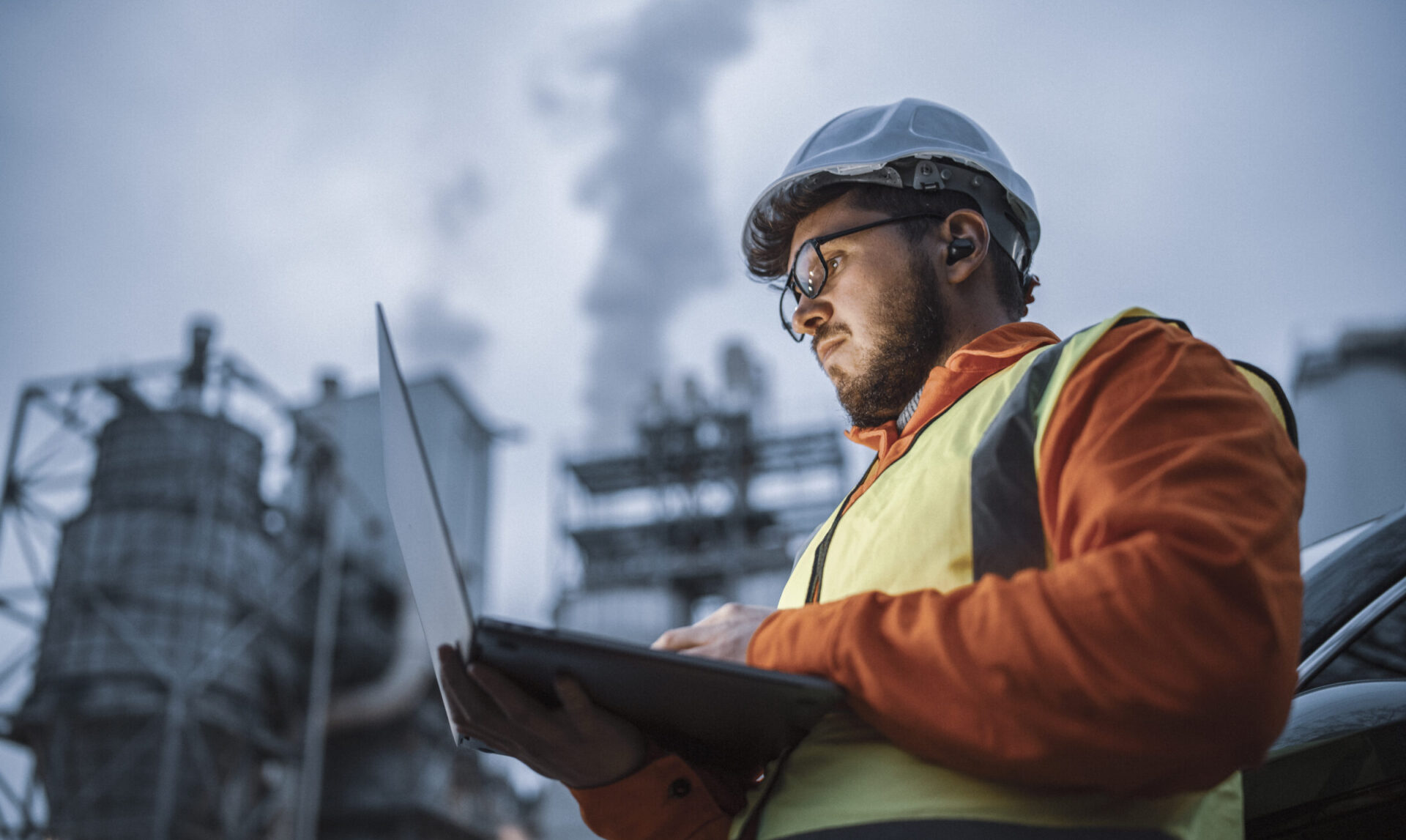 Man met veiligheidskleding en laptop aan het werk op een industrieterrein