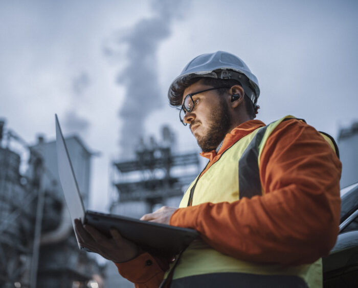 Man met veiligheidskleding en laptop aan het werk op een industrieterrein