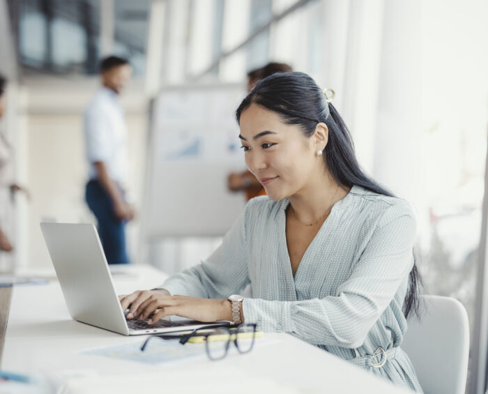 Vrouw aan het werk achter haar laptop met collega's op de achtergrond